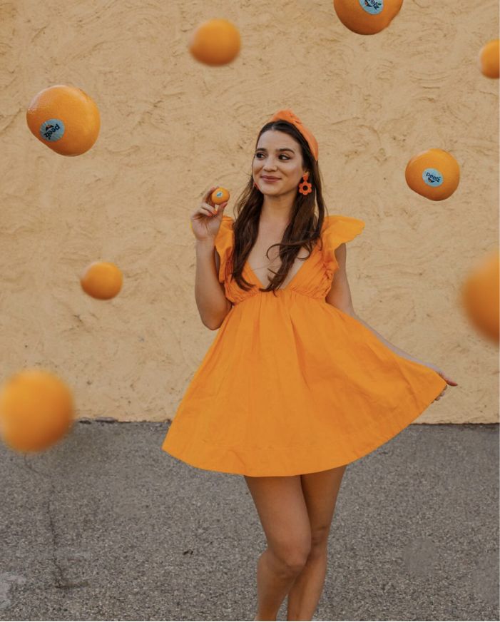 A woman in an orange dress with Peelz seedless California mandarins falling around her.