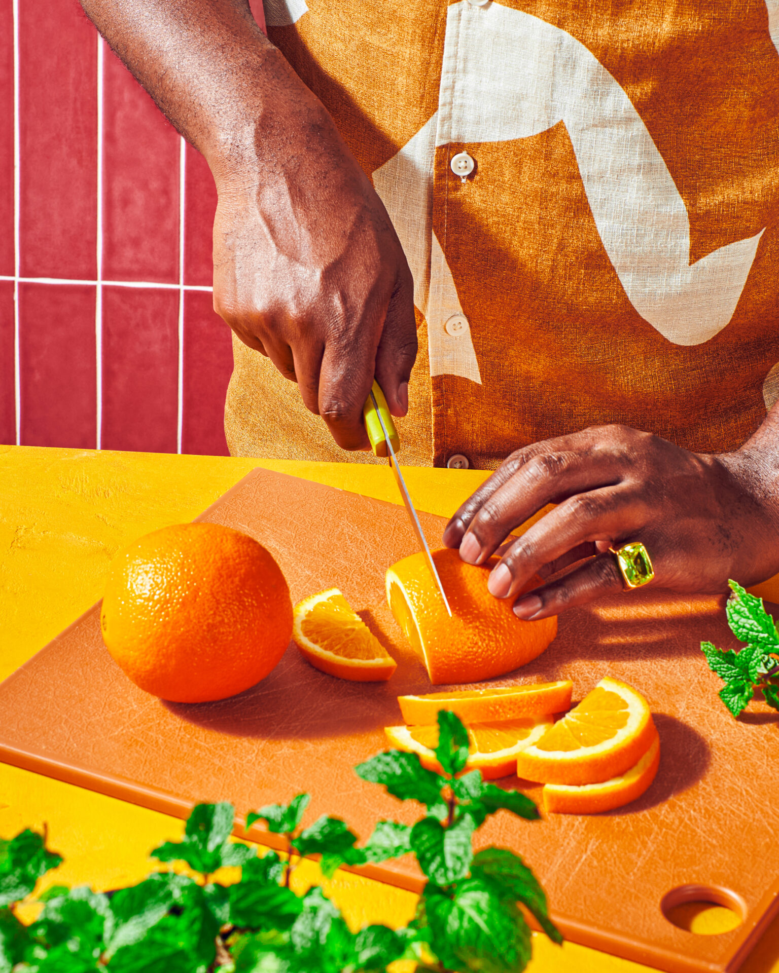 Hand slicing a Peelz orange on a cutting board with mint